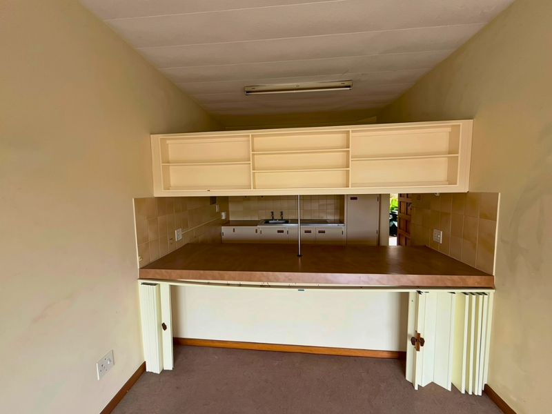 A dated kitchen area featuring built-in cabinetry, a laminate breakfast bar, and tiled backsplash, currently vacant and ready for renovation.