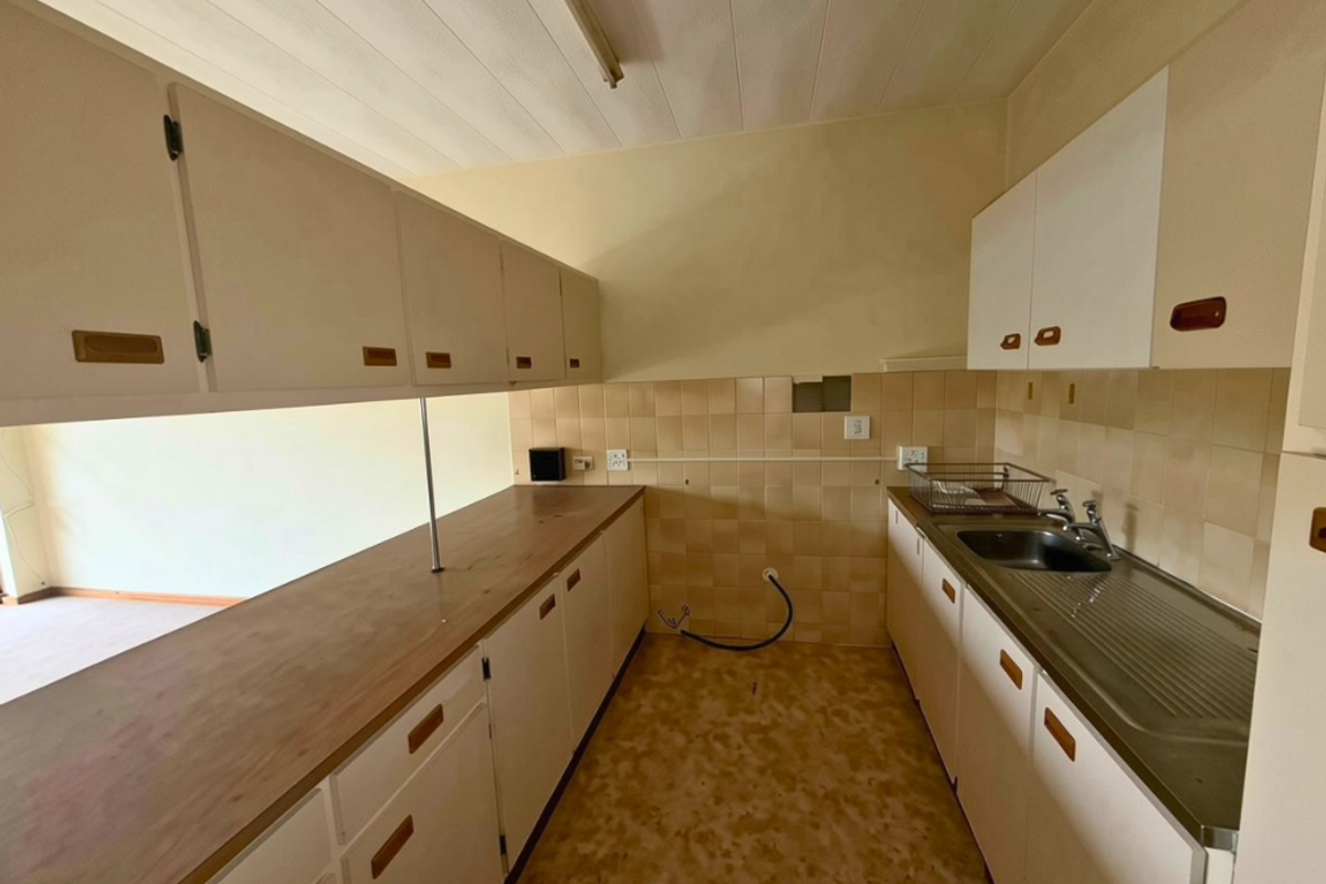 A dated kitchen featuring original cabinetry, laminate countertops, and a stainless steel sink, requiring modernization to improve functionality and aesthetic appeal.