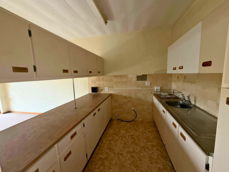 A dated kitchen featuring original cabinetry, laminate countertops, and a stainless steel sink, requiring modernization to improve functionality and aesthetic appeal.