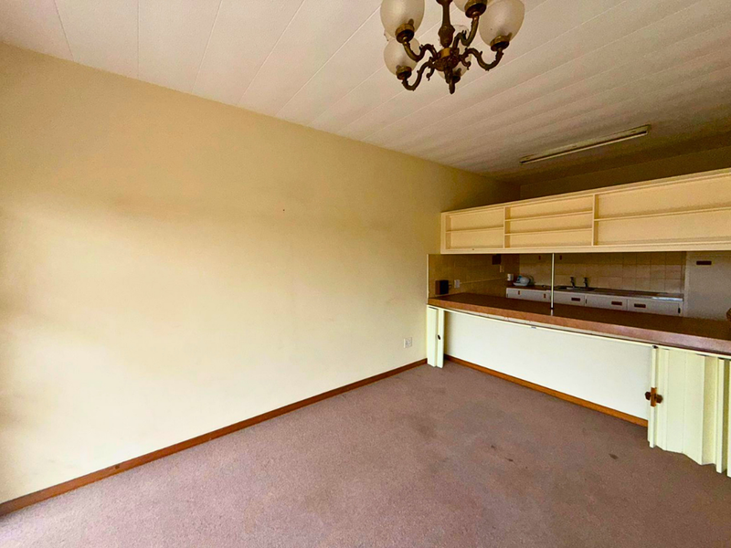 An open-plan living and kitchen area featuring dated cabinetry, a built-in counter, and carpeted flooring, offering a blank canvas for renovation.