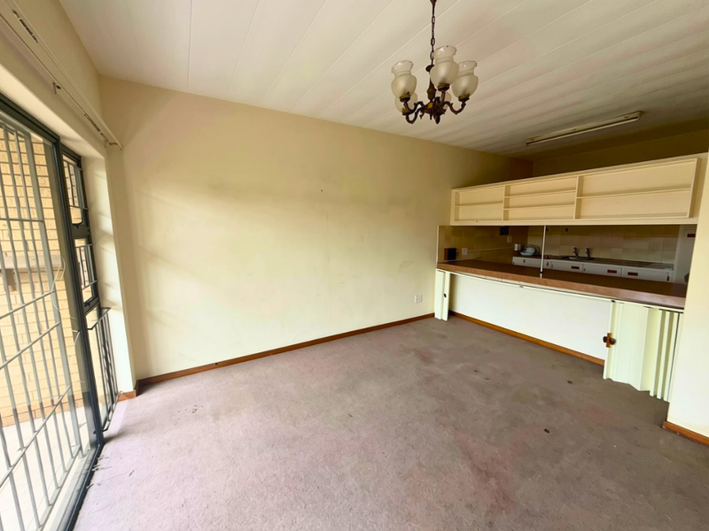 An empty open-plan living and kitchen area featuring dated cabinetry, a breakfast counter, and direct access to an outdoor space via a sliding door.