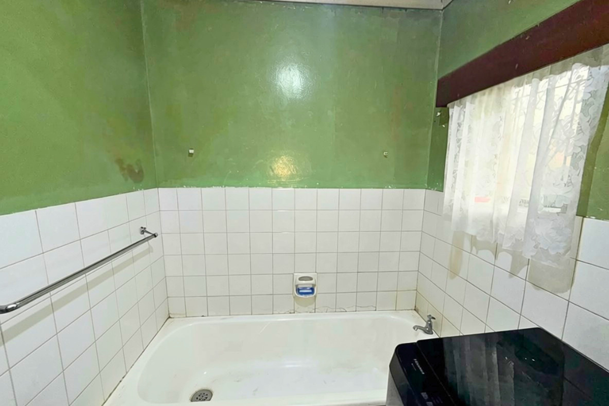 A dated bathroom featuring a built-in bathtub with white tiled splashbacks and green painted walls, requiring cosmetic updates and maintenance.