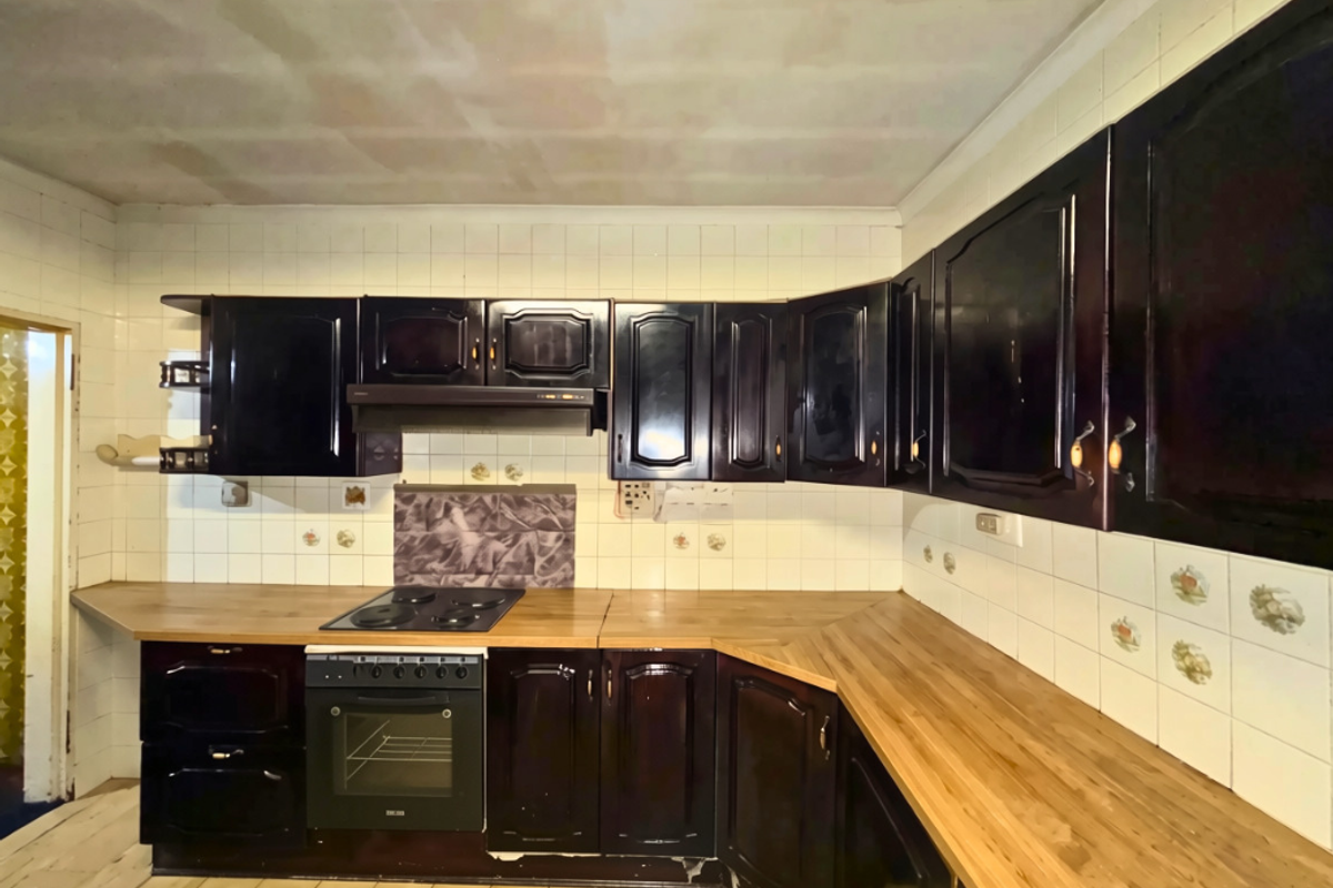 A dated kitchen featuring dark cabinetry, wooden countertops, and an integrated oven and hob, requiring cosmetic updates to modernize the space.