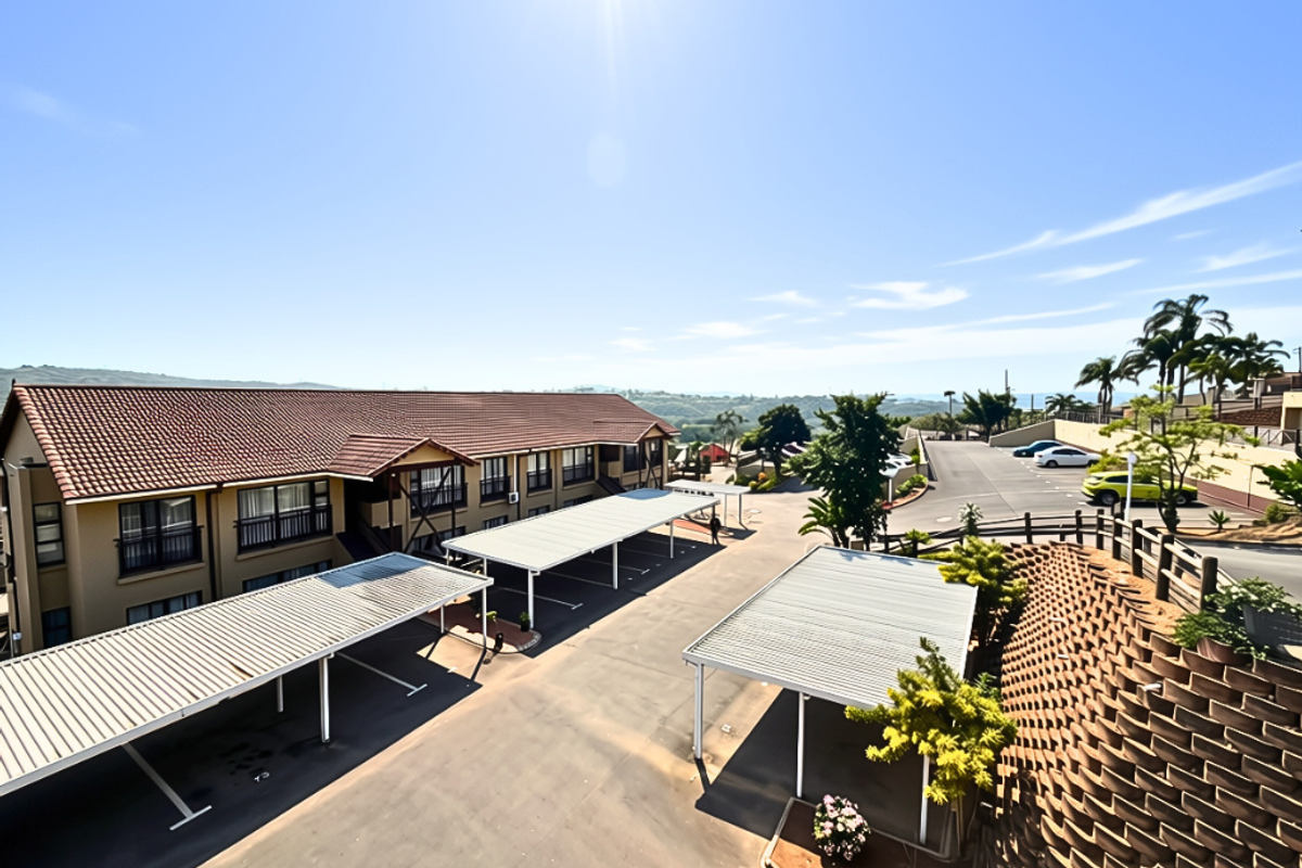 Aerial view of the apartment complex featuring covered parking bays, paved driveway, and a structured retaining wall with surrounding landscaping.