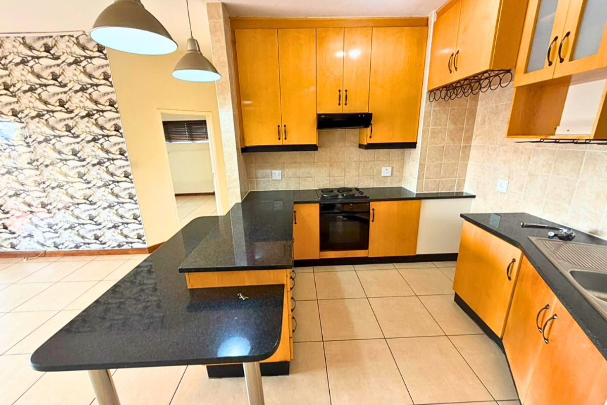 A functional kitchen featuring wooden cabinetry, granite countertops, a built-in oven with gas hob, and a breakfast bar, finished with tiled flooring and backsplash.