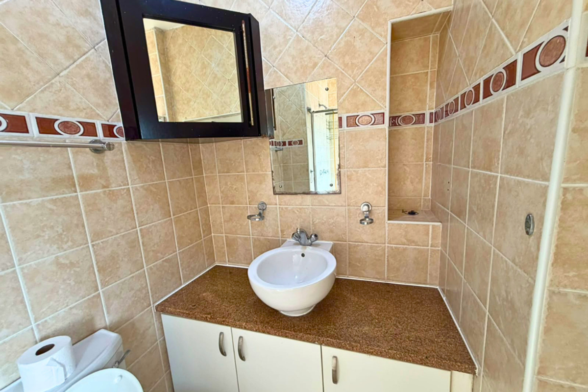 A compact bathroom featuring a vessel sink on a granite vanity, tiled walls with decorative accents, and a built-in wall niche for storage.