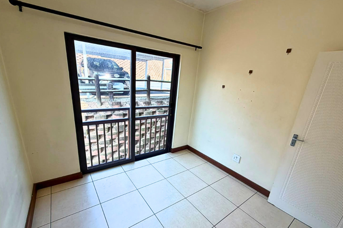 An empty bedroom featuring tiled flooring and a sliding glass door providing access to the exterior.