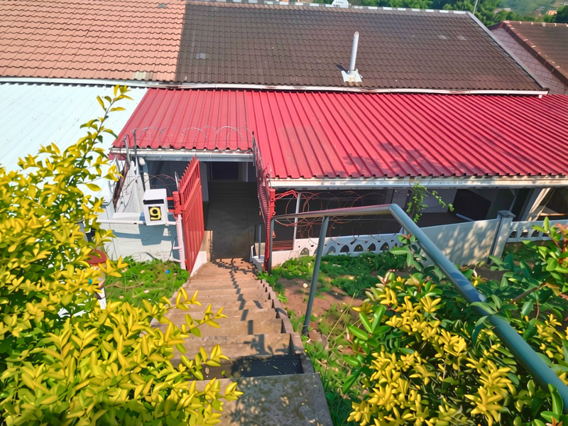 Front entrance view featuring a concrete staircase with metal handrails, leading to a property with a combination of tiled and metal roofing.
