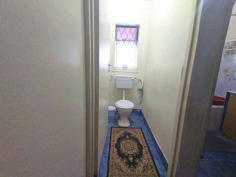 A compact, functional bathroom featuring a standard toilet, tiled flooring, and a leaded glass window, offering a dated but practical layout.