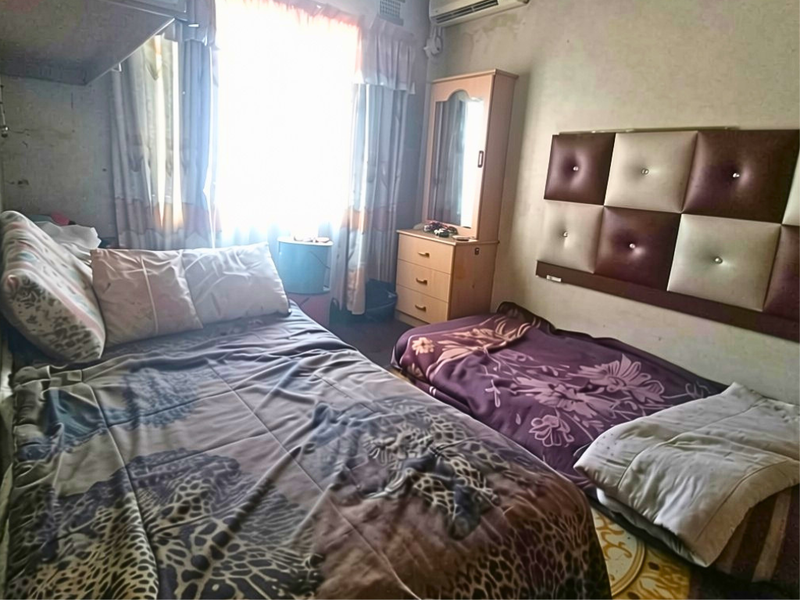 A bedroom featuring an air conditioning unit and a wall-mounted headboard, showing signs of wear on the walls requiring maintenance.