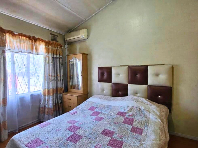A bedroom featuring a vaulted ceiling, split-system air conditioning unit, and security bars on the window, requiring cosmetic updates to the wall and ceiling finishes.