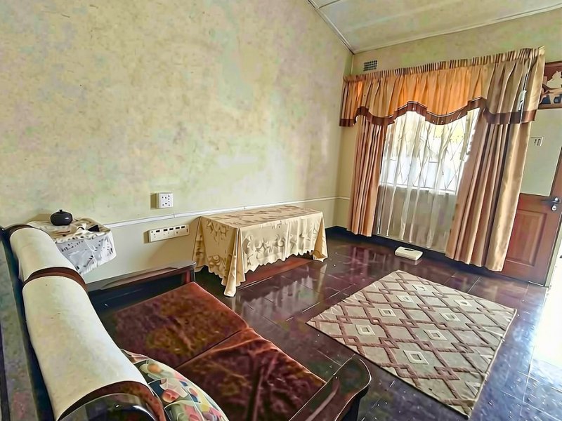A living room featuring tiled flooring, security gate, and dated wall finishes, offering potential for modernization and aesthetic improvement.