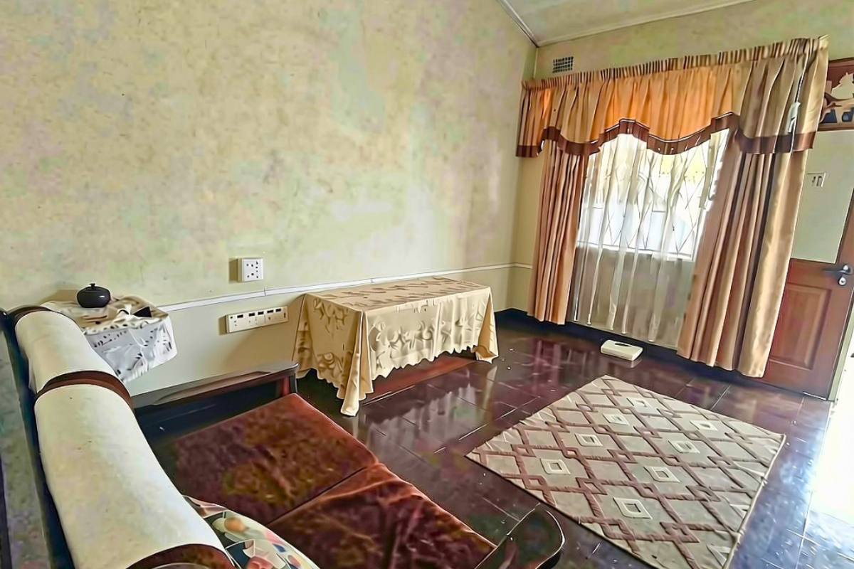 A living room featuring tiled flooring, security gate, and dated wall finishes, offering potential for modernization and aesthetic improvement.