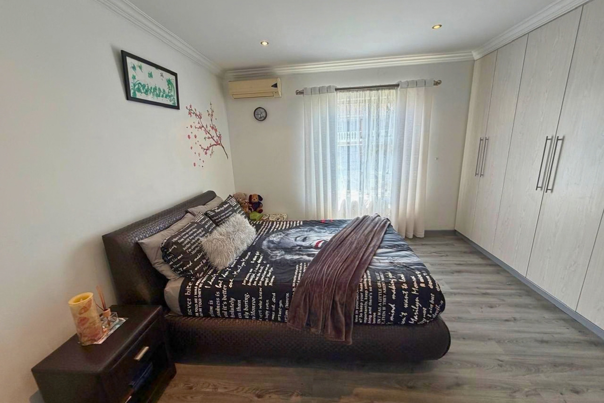 A well-maintained bedroom featuring built-in cupboards, laminate flooring, recessed downlights, and an integrated air conditioning unit.