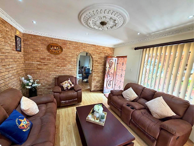 A living room featuring an exposed brick feature wall, decorative ceiling rose, cornice detailing, and laminate flooring, with an arched transition to an adjacent space.