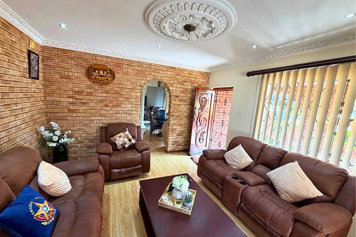 A living room featuring an exposed brick feature wall, decorative ceiling rose, cornice detailing, and laminate flooring, with an arched transition to an adjacent space.