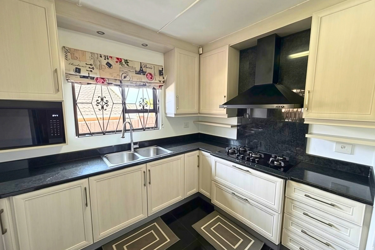 A well-maintained kitchen featuring light-toned cabinetry, dark granite countertops, a gas hob with extractor fan, and a built-in microwave.