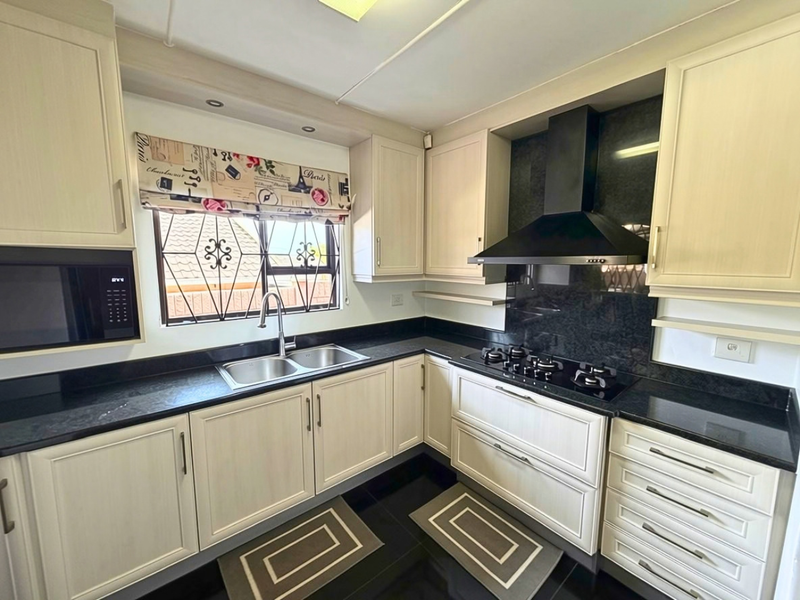 A well-maintained kitchen featuring light-toned cabinetry, dark granite countertops, a gas hob with extractor fan, and a built-in microwave.