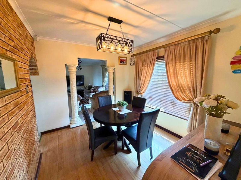 A well-lit dining room featuring an exposed brick feature wall, decorative columns, laminate flooring, and a modern industrial-style pendant light fixture.