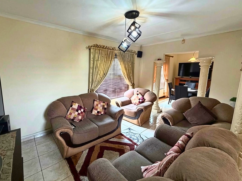 A living room featuring tiled flooring, decorative columns, and modern pendant lighting, with an open transition to the adjacent dining area.