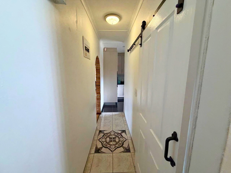 A narrow hallway featuring tiled flooring with a decorative inlay, a sliding barn door, and an arched transition leading to the kitchen area.