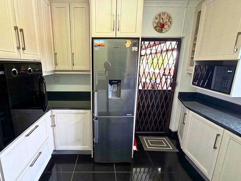Modern kitchen featuring light shaker-style cabinetry, dark granite countertops, built-in oven and microwave, and sleek black floor tiles with a security gate exit.