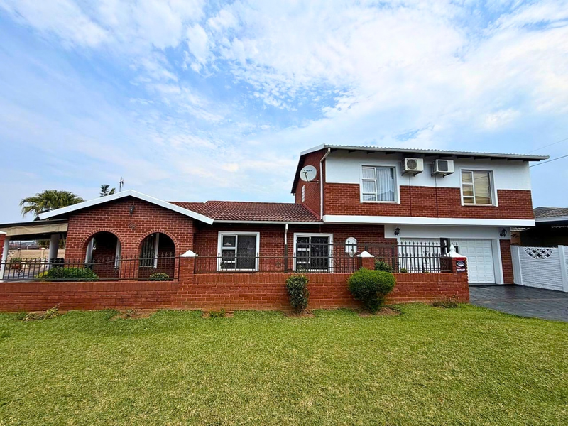 A well-maintained double-story brick house featuring a tiled roof, arched entryway, integrated garage, and a neat front lawn with perimeter fencing.