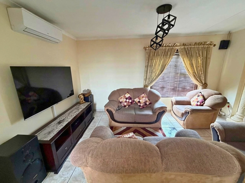 A comfortable living room featuring tiled flooring, a wall-mounted air conditioning unit, and a contemporary pendant light fixture.