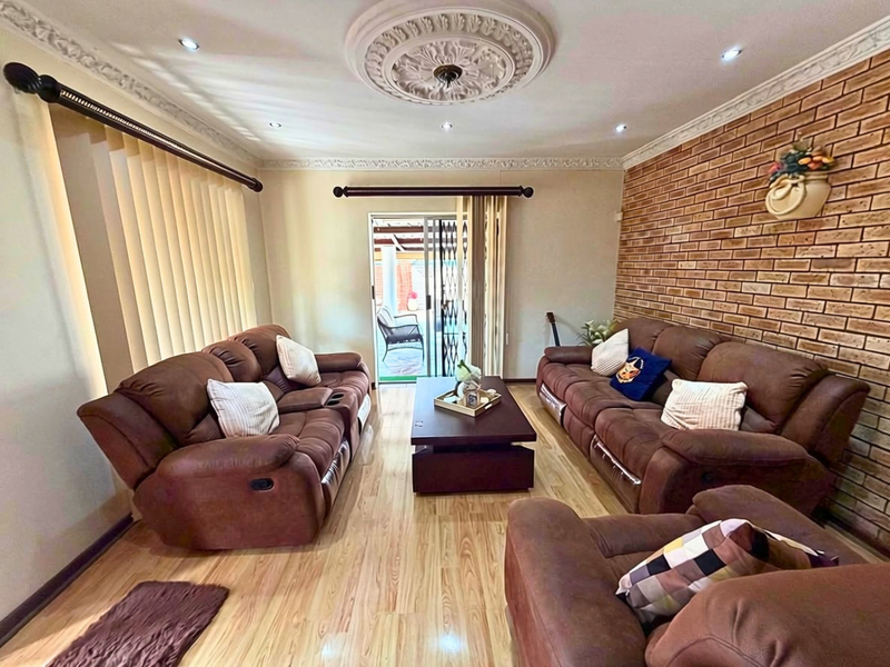 A well-maintained living room featuring an exposed brick accent wall, decorative ceiling rose, recessed lighting, and laminate flooring with direct access to the patio.