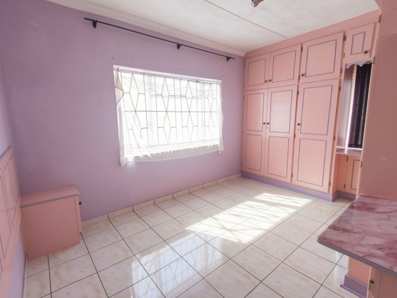 An empty bedroom featuring built-in cupboards, tiled flooring, and security bars on the window, offering a blank canvas for renovation.