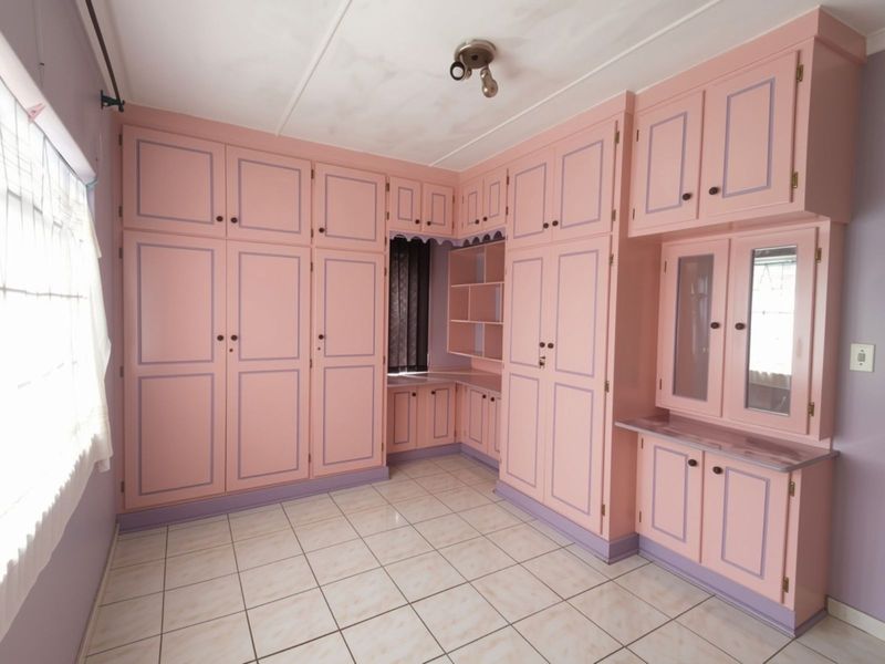 A bedroom featuring extensive built-in cabinetry with a dated pink and purple finish, tiled flooring, and a built-in vanity area.