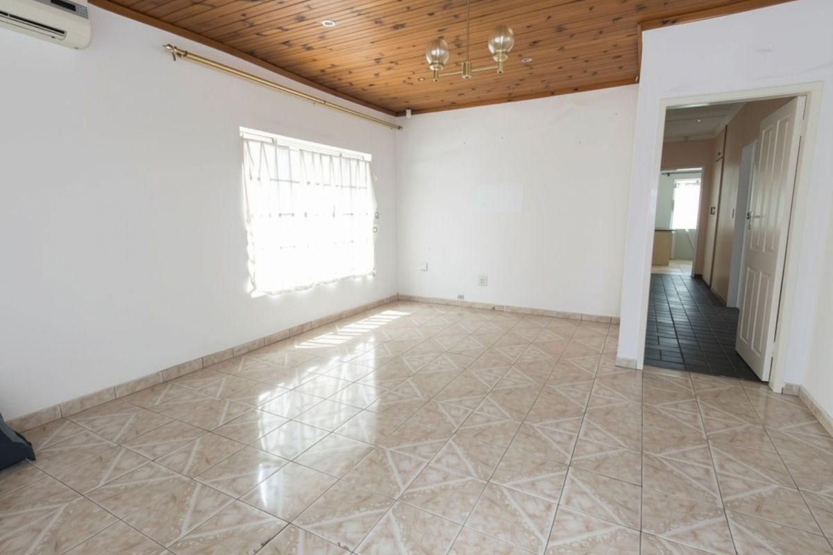 An empty living room featuring ceramic floor tiles, a timber tongue and groove ceiling, and a wall-mounted air conditioning unit.