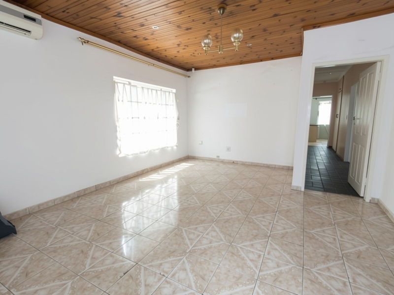 An empty living room featuring ceramic floor tiles, a timber tongue and groove ceiling, and a wall-mounted air conditioning unit.