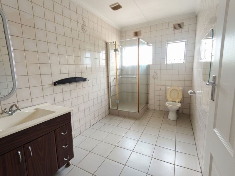 A functional bathroom featuring a vanity cabinet, a glass-enclosed shower, and a toilet, finished with neutral wall and floor tiles.