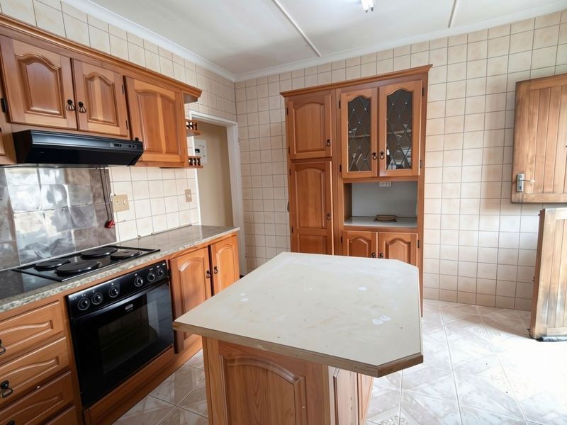 A functional kitchen featuring traditional wooden cabinetry, a built-in electric stove with extractor fan, tiled backsplash, and a central kitchen island.