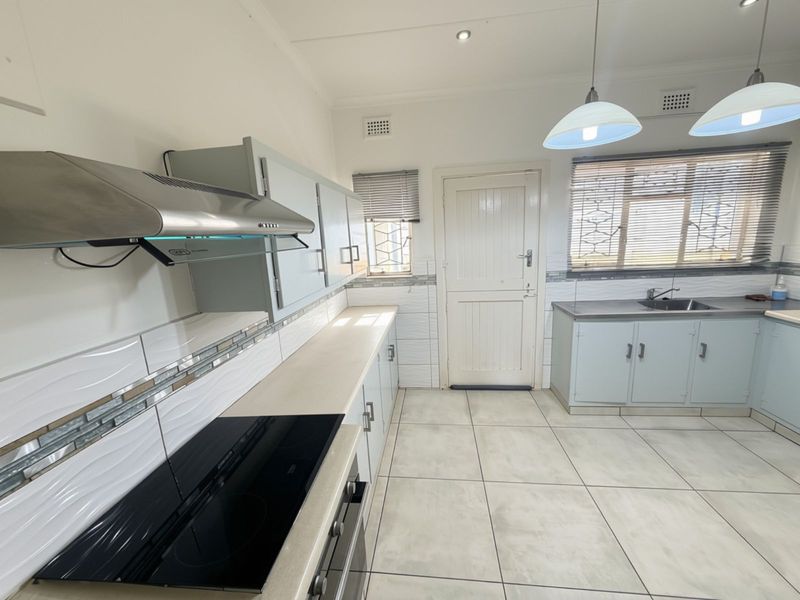 A clean, functional kitchen featuring built-in cabinetry, an electric hob, extractor fan, and tiled flooring with a neutral backsplash.