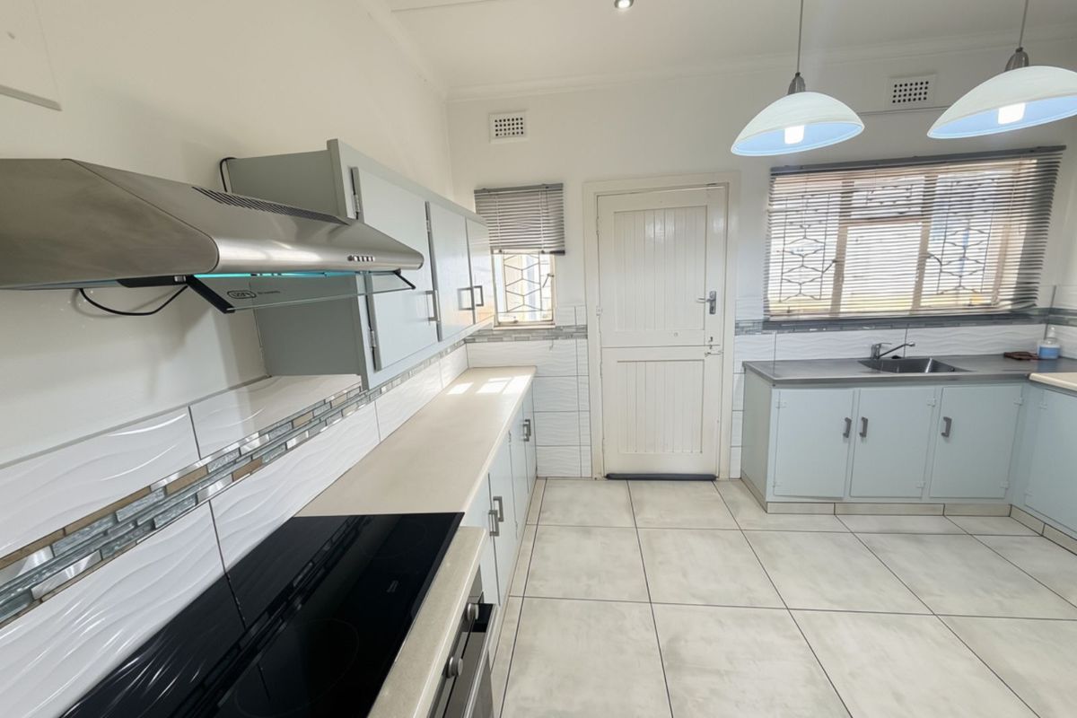 A clean, functional kitchen featuring built-in cabinetry, an electric hob, extractor fan, and tiled flooring with a neutral backsplash.