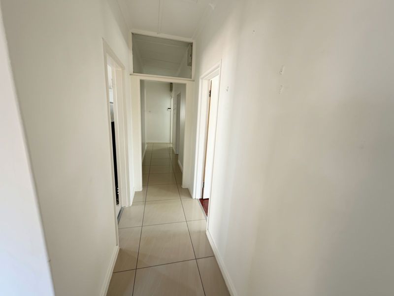 A clean, empty hallway featuring neutral tiled flooring and multiple doorways leading to adjacent rooms.