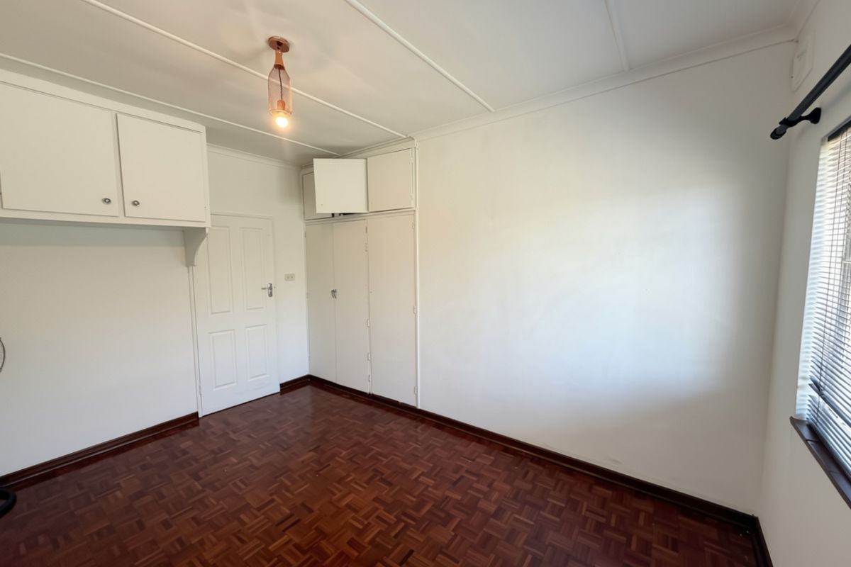 An empty bedroom featuring classic parquet flooring, built-in storage cupboards, and a neutral color palette, ready for personalization.