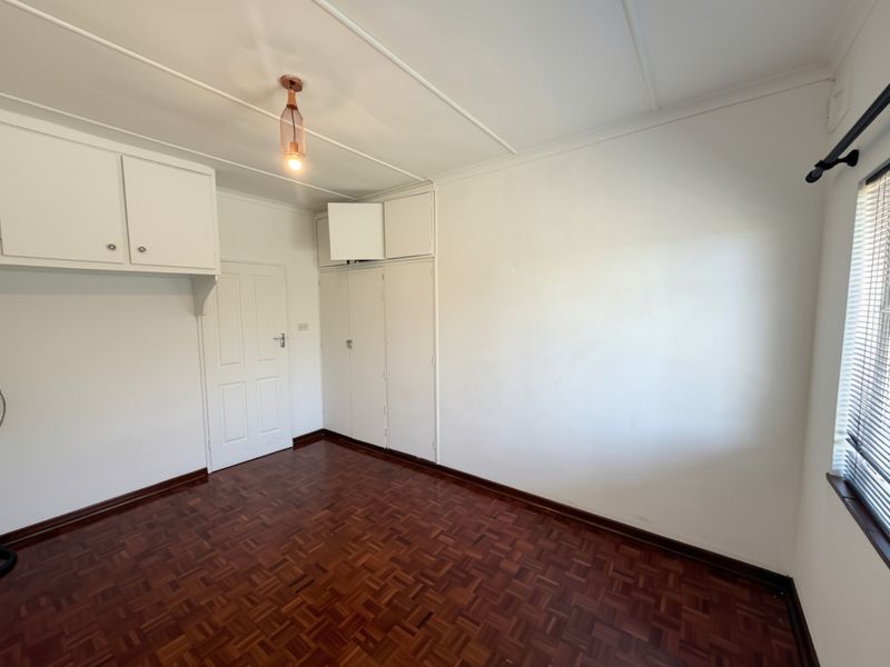 An empty bedroom featuring classic parquet flooring, built-in storage cupboards, and a neutral color palette, ready for personalization.