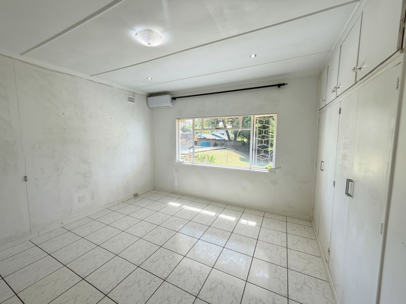 An empty bedroom featuring tiled flooring, built-in cupboards, and an air conditioning unit, offering a blank canvas for personalization.