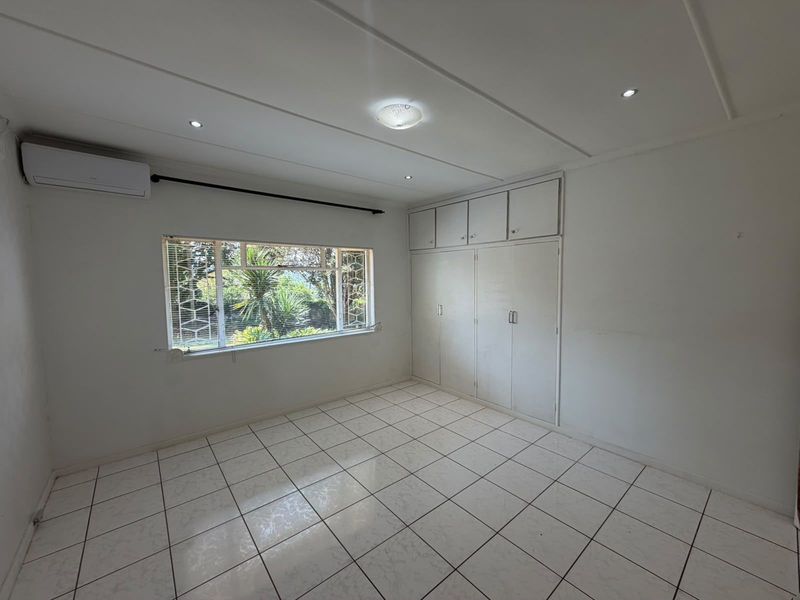 A bright, empty bedroom featuring tiled flooring, built-in cupboards, and an installed air conditioning unit, offering a clean canvas for personalization.