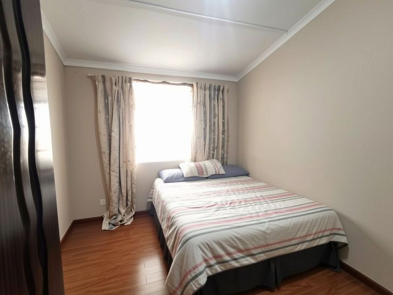 A standard bedroom featuring laminate flooring, neutral wall paint, and a window with curtains.