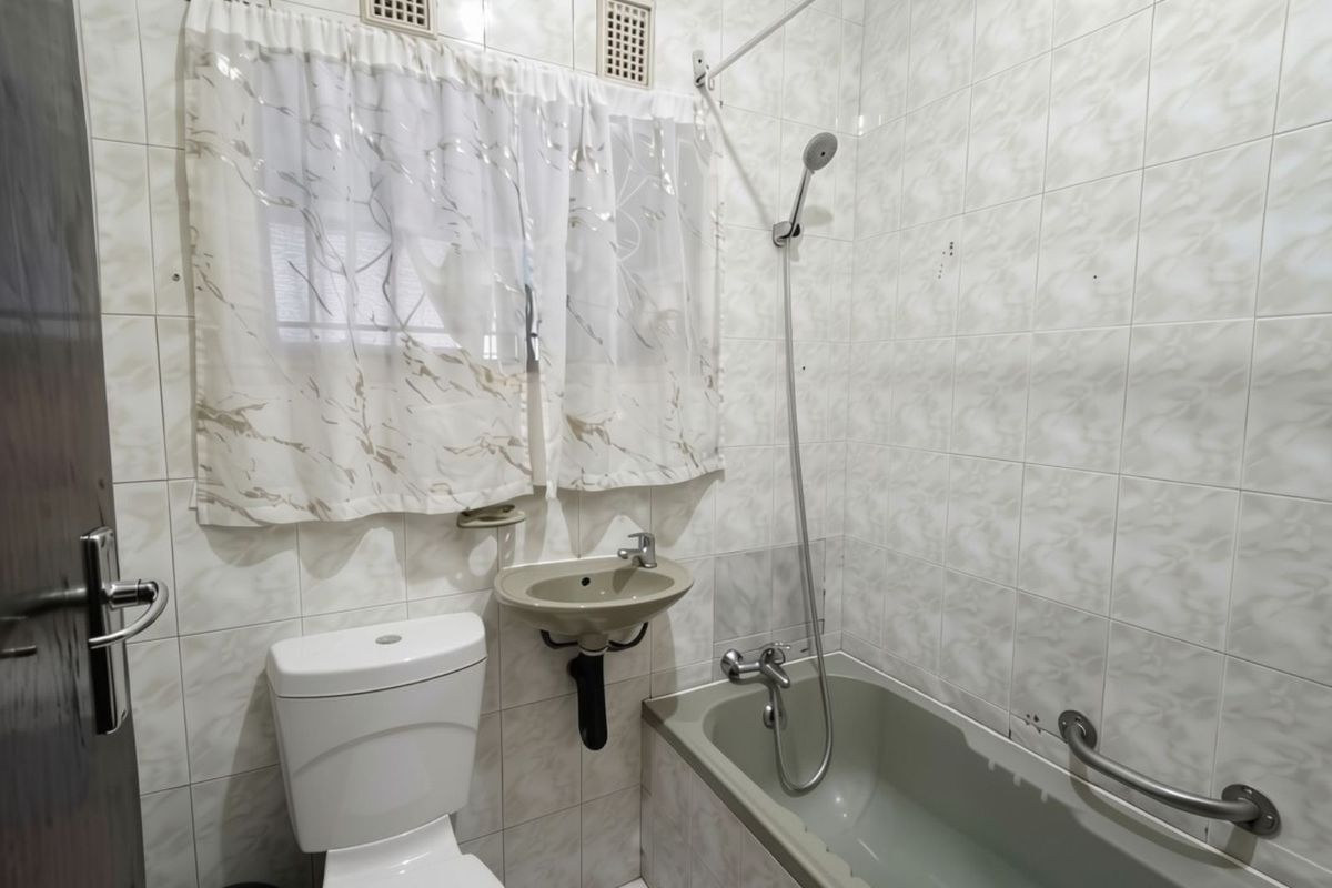 A functional bathroom featuring a bathtub with handheld shower, wall-mounted basin, and toilet, finished with full-height wall tiling.