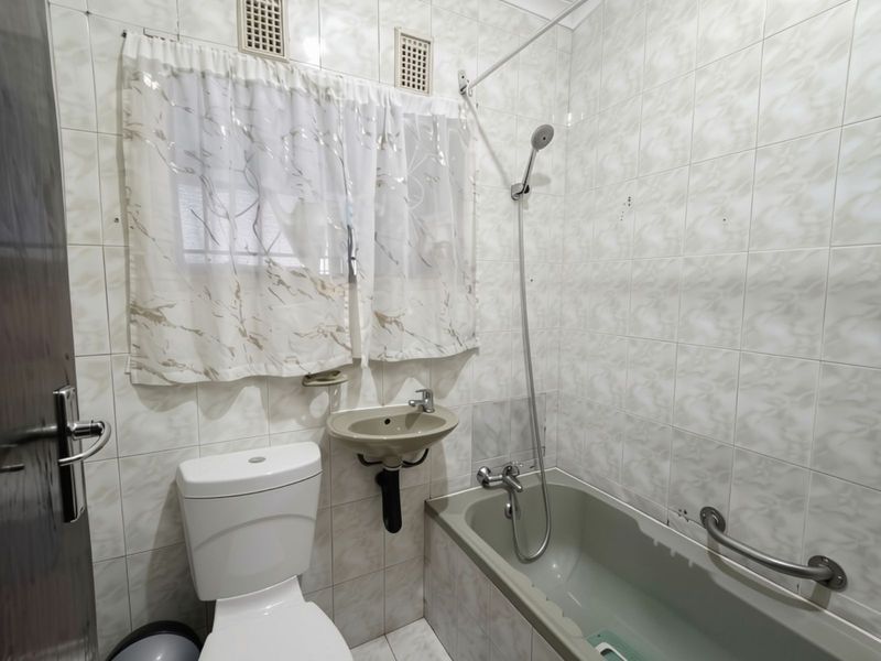 A functional bathroom featuring a bathtub with handheld shower, wall-mounted basin, and toilet, finished with full-height wall tiling.