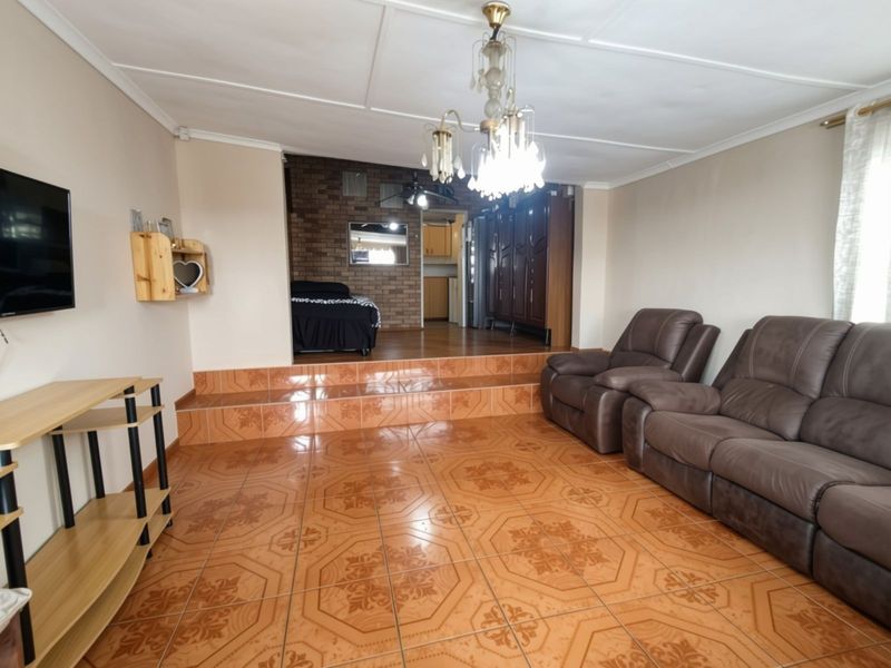 Spacious living area featuring a raised platform, decorative tiled flooring, and an exposed brick feature wall leading to an adjacent kitchen space.