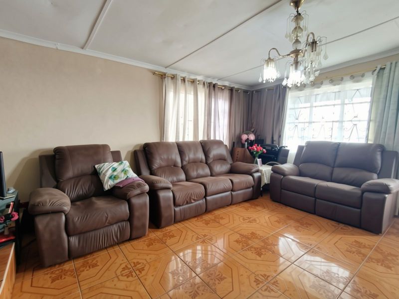 A living room featuring ceramic tile flooring, a decorative chandelier, and windows fitted with security bars.