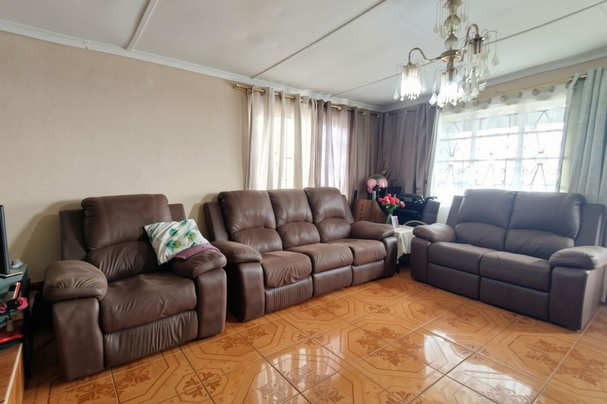 A living room featuring ceramic tile flooring, a decorative chandelier, and windows fitted with security bars.