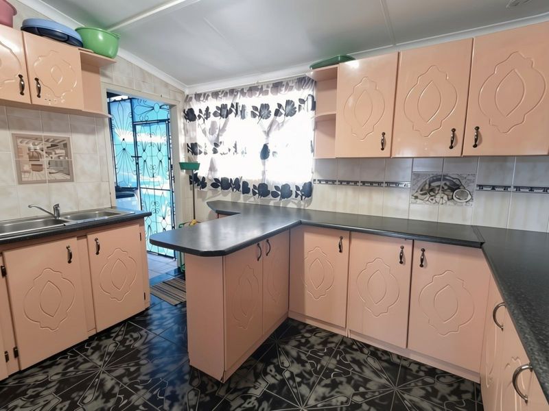 A functional kitchen featuring pink cabinetry, dark laminate countertops, tiled flooring, and a tiled backsplash with a convenient side entrance.