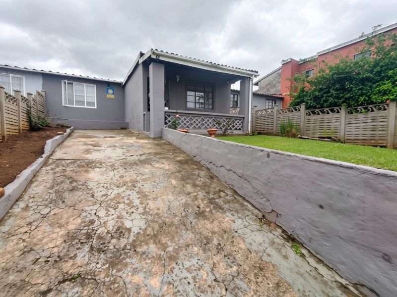 Front exterior view of the house featuring a concrete driveway, a covered porch area, and a precast boundary wall with a small lawn.